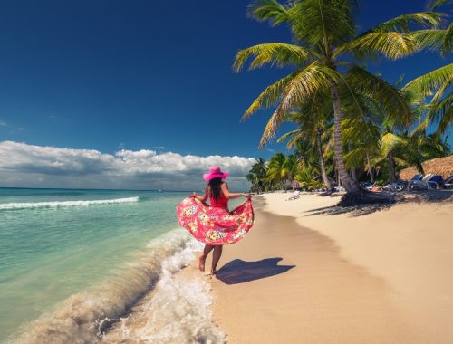 Mujer caminando descalza sobre la arena del Caribe frente al mar.