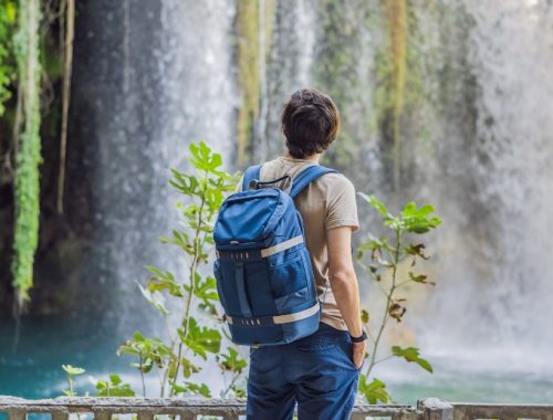 Hombre de espaldas con mochila observando la vista de una cascada