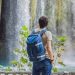 Hombre de espaldas con mochila observando la vista de una cascada