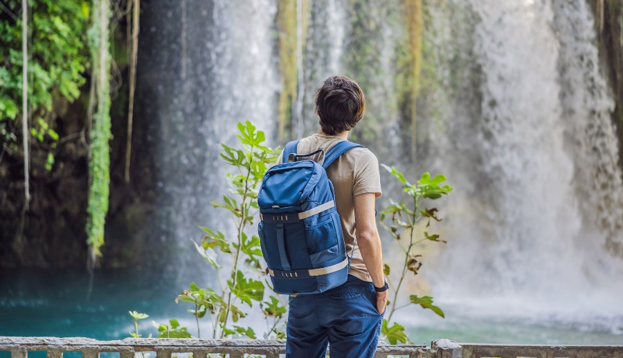 Hombre de espaldas con mochila observando la vista de una cascada