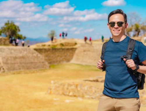 Hombre sosteniendo las correas de la mochila y sonriendo para una foto en una ciudad antigua