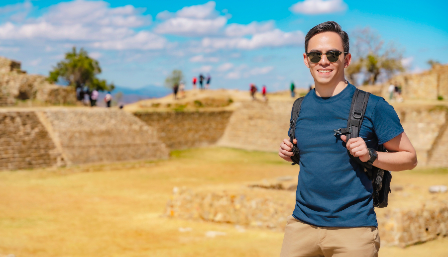Hombre sosteniendo las correas de la mochila y sonriendo para una foto en una ciudad antigua