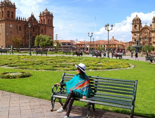 Mujer sentada en un banco frente a un sitio turístico en Perú