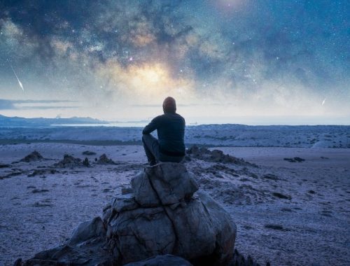 Hombre sentado sobre una roca observando el cielo colorido con lluvia de meteoros