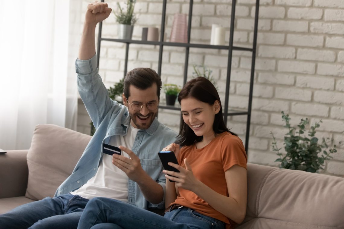 Pareja sosteniendo una tarjeta de crédito, celebrando la compra de un boleto barato desde el celular.