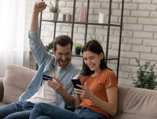 Pareja sosteniendo una tarjeta de crédito, celebrando la compra de un boleto barato desde el celular.