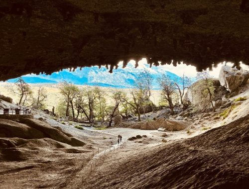 Dos personas saliendo de la Cueva del Milodón frente a árboles y montañas.