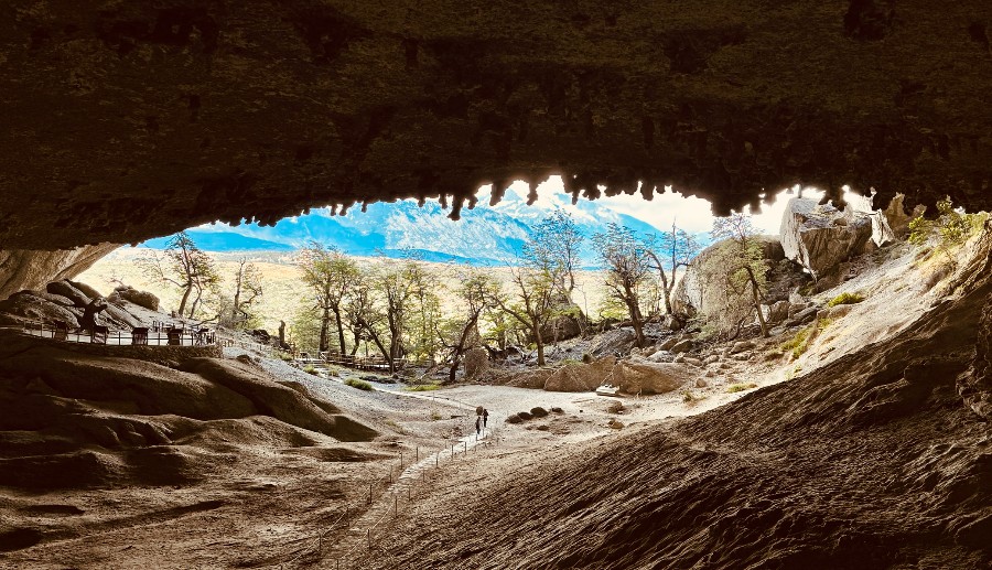 Dos personas saliendo de la Cueva del Milodón frente a árboles y montañas.