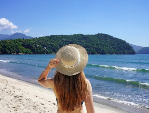 Mujer de espaldas observando la playa de Ilhabela con un sombrero en la cabeza