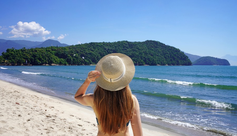 Mujer de espaldas observando la playa de Ilhabela con un sombrero en la cabeza