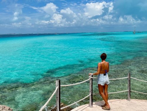 Mujer observando el mar con aguas cristalinas en un día soleado