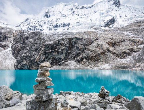 Imagen de paisaje con montañas y un lago azul cristalino con algunas rocas apiladas