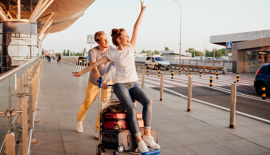Pareja divirtiéndose mientras transporta las maletas en el aeropuerto