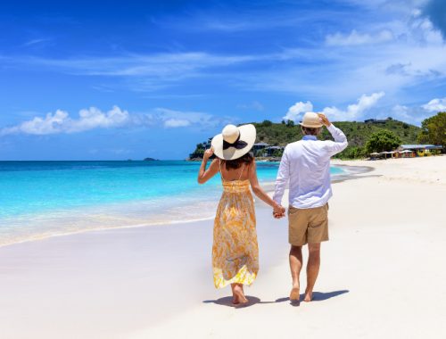 Pareja caminando por la playa de la mano con vista a aguas cristalinas