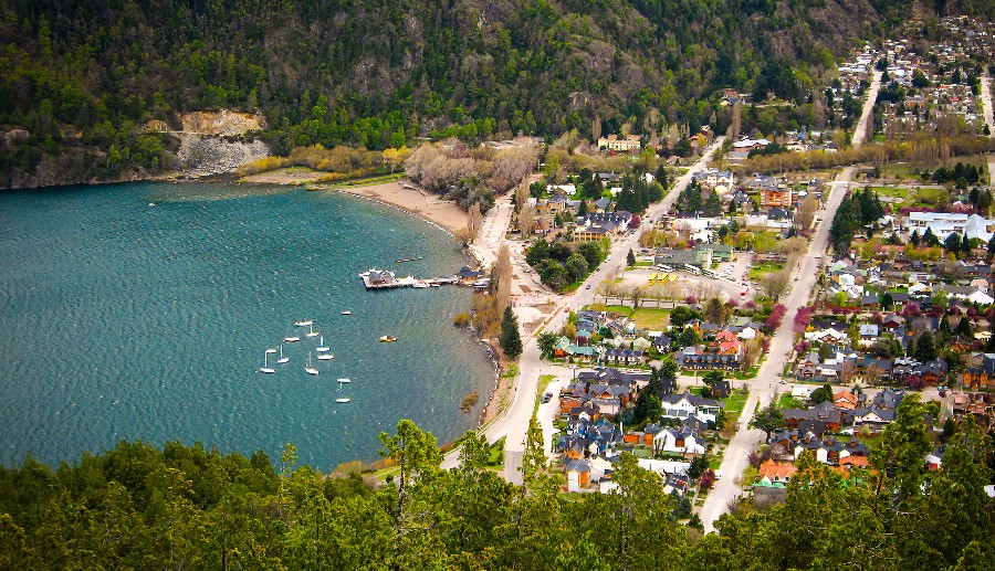 Foto de un pequeño pueblo rodeado de montañas, árboles y mar con aguas cristalinas