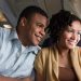 Pareja heterosexual dentro de un avión observando la vista con una sonrisa en el rostro