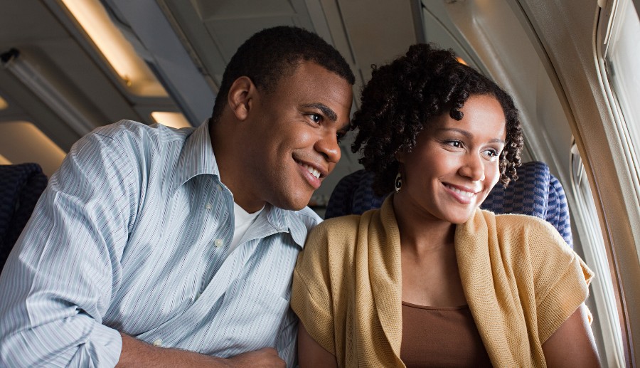 Pareja heterosexual dentro de un avión observando la vista con una sonrisa en el rostro