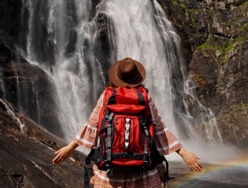 Mujer con mochila en la espalda posando para una foto frente a una cascada