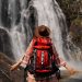 Mujer con mochila en la espalda posando para una foto frente a una cascada