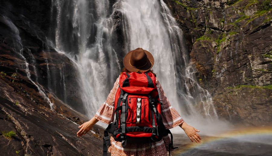 Mujer con mochila en la espalda posando para una foto frente a una cascada