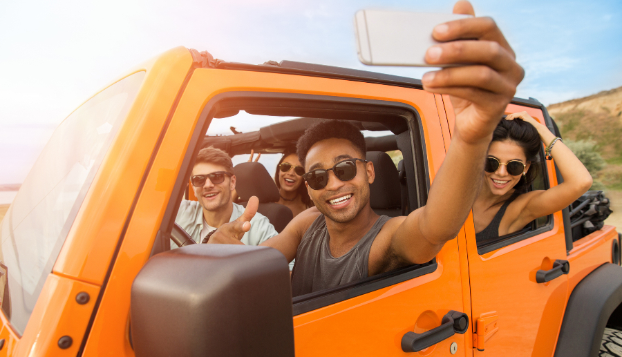 Grupo de amigos dentro de un mini auto naranja posando para una selfie