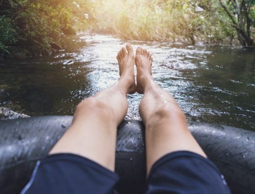 Hombre con los pies fuera del flotador practicando tubing en un río