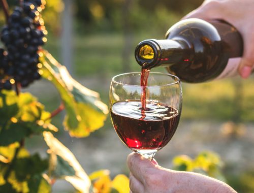 Mujer llenando una copa de vino frente a un viñedo